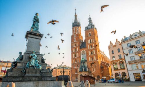 Old city center view with Adam Mickiewicz monument, St. Mary's Basilica and birds flying in Krakow on the morning